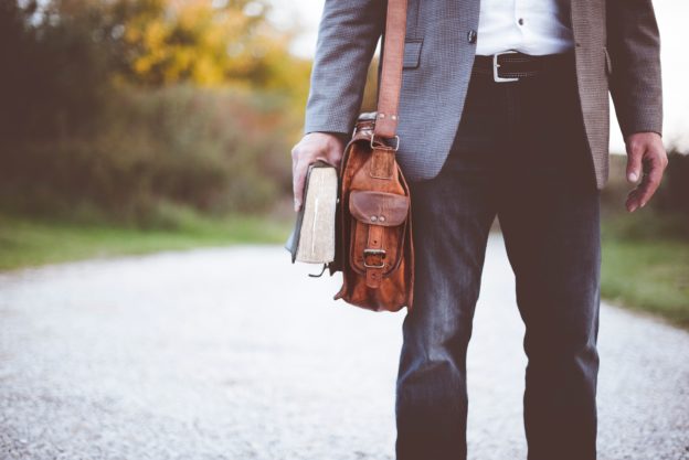 Imagem de um homem com uma bolsa e um livro em uma estrada
